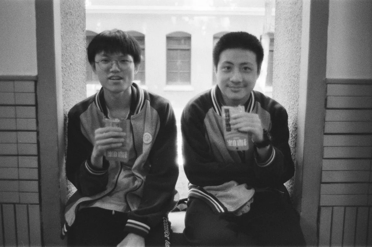 两名学生坐在窗边，手持饮料看向镜头