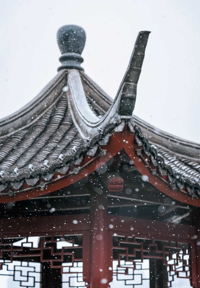 大雪掠过灰瓦红柱的中式亭子